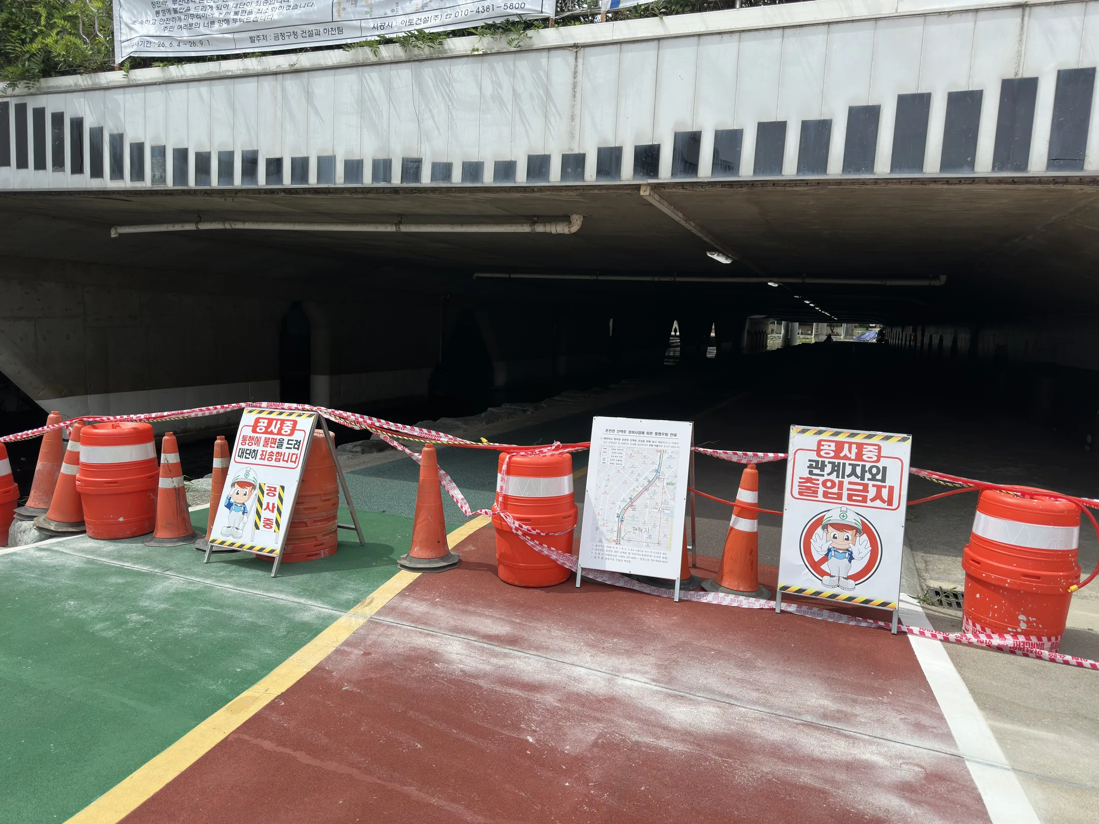 Construction barrels and signs blocking the Oncheoncheon bicycle path under the Jangjeon Station area