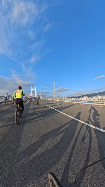 Cyclists riding toward white bridge towers under a blue sky