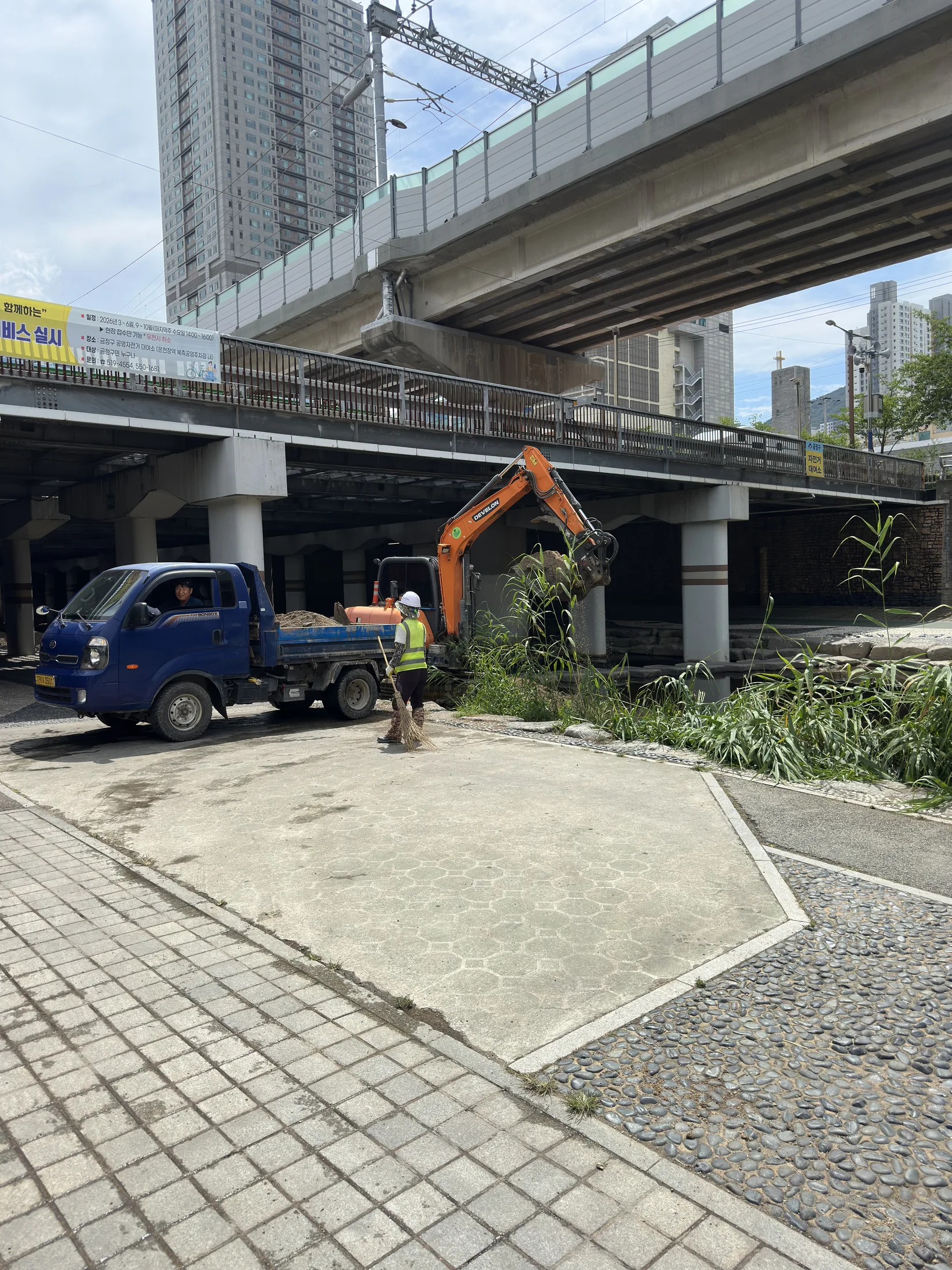 Excavator and worker beside the upper Oncheoncheon path under the rail viaduct